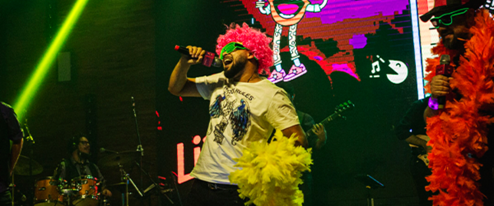 Cantora de banda de karaokê se apresenta para uma plateia engajada com mãos ao alto. A cena é iluminada por luzes de palco vibrantes, transmitindo uma atmosfera de entretenimento e festa interativa.